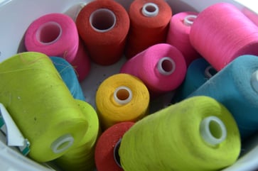 A collection of colorful sewing thread bobbins in a white bowl