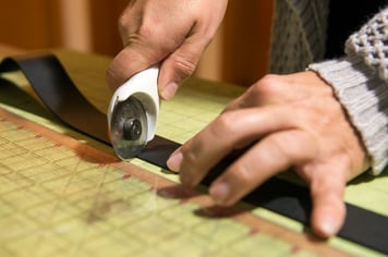 Jewelry maker cutting a leather strap for a cuff bracelet with a rotary cutter and a cutting mat