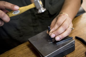 Jewelry maker hand stamping a piece of metal with a hammer