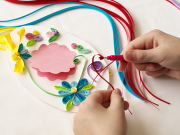 Paper crafter rolling strips of paper to make a floral card design