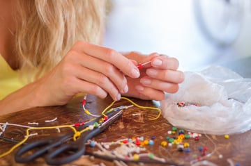 Jewelry maker stringing beads using pliers and a needle