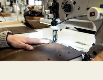 Maker who sews using a sewing machine on dark brown leather