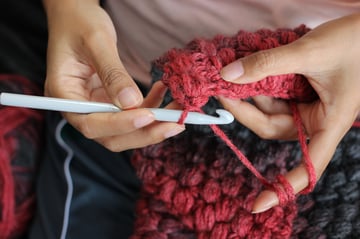 Fiber artist crocheting with red yarn and a hook