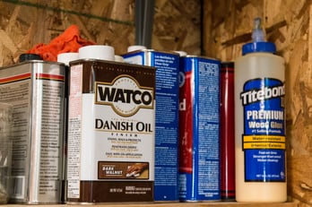 Wood oil and adhesive products that woodworkers use on a shelf in a workshop