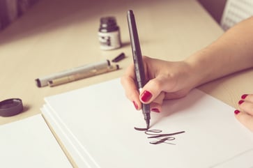 Calligrapher hand lettering on cardstock with a large brush and black ink