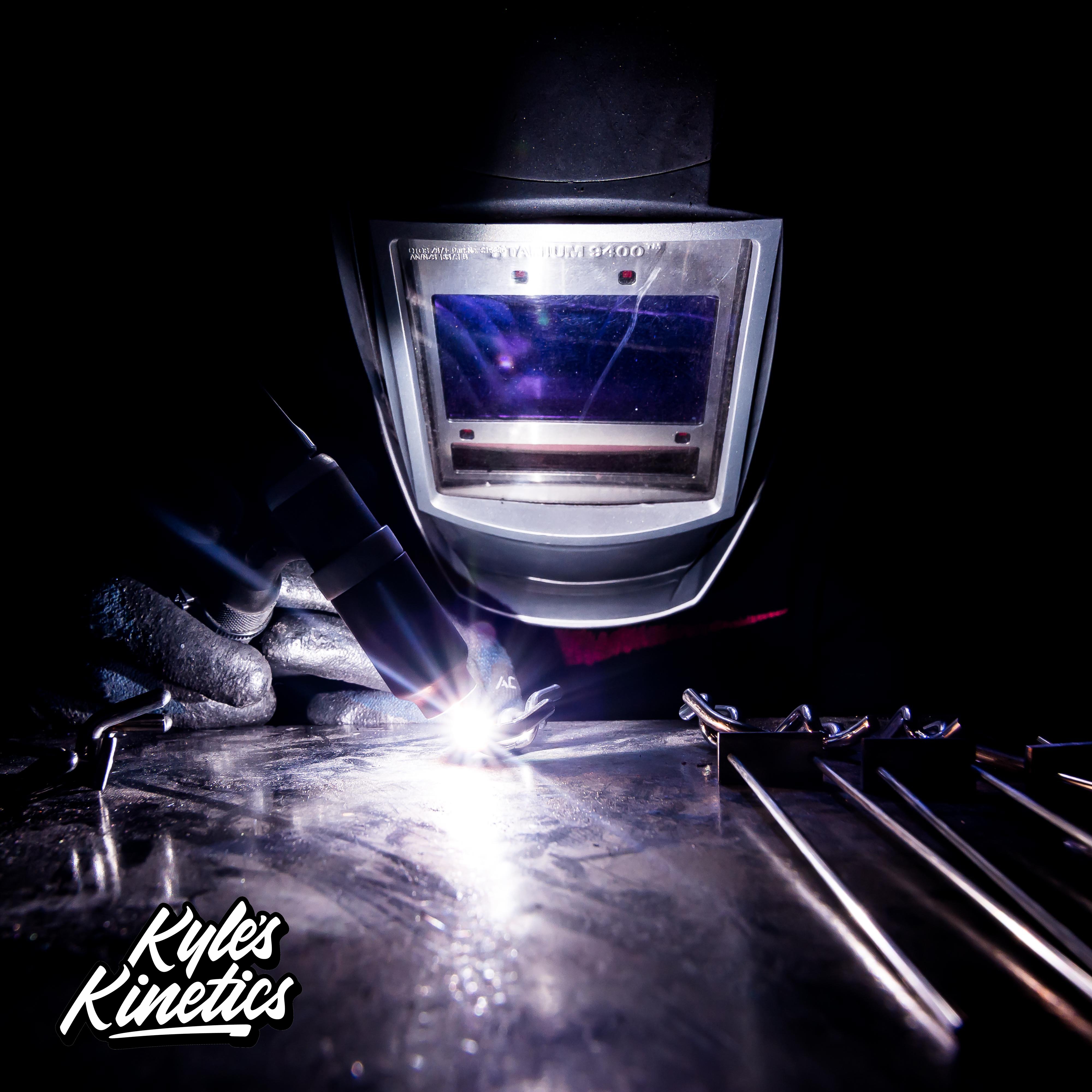 Kyle of Kyle's Kinetics welding stainless steel balancing sculptures in a welding mask